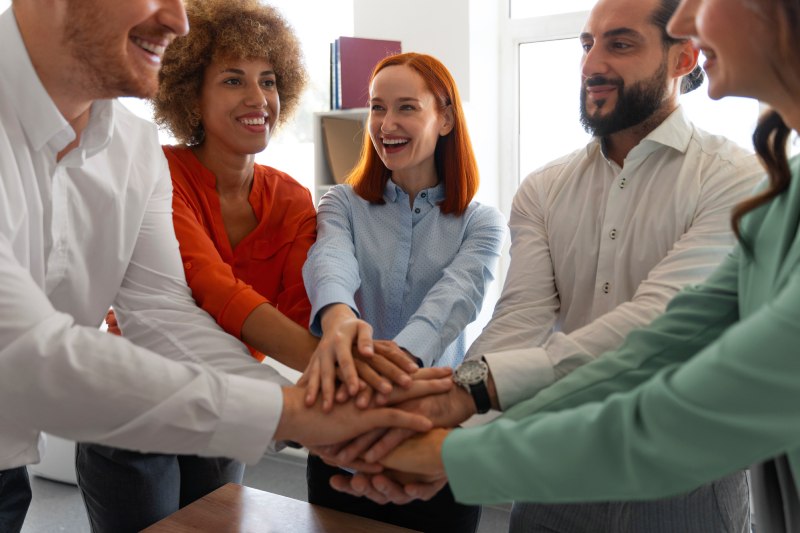 Des partenaires souriants réunis en cercle, plaçant leurs mains au centre pour symboliser leur engagement commun à renforcer leur réseau. L'mage reflète l'esprit d'équipe et l'entraide qui sont essentiels pour cultiver des relations durables et réussies dans le monde professionnel.