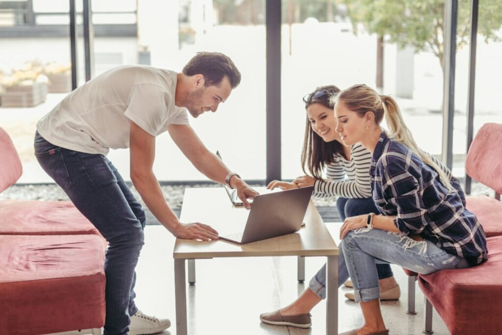 Un homme présente son pitch en face de deux femmes ciblées par sa stratégie commerciale. Le bureau bien éclairé crée un cadre professionnel propice à la communication. L'enthousiasme de l'homme et l'attention soutenue des deux femmes témoignent de l'importance de l'engagement et de la connexion personnelle dans le processus commercial. La scène reflète l'essence même d'une approche centrée sur le client et de la recherche de relations solides et durables.