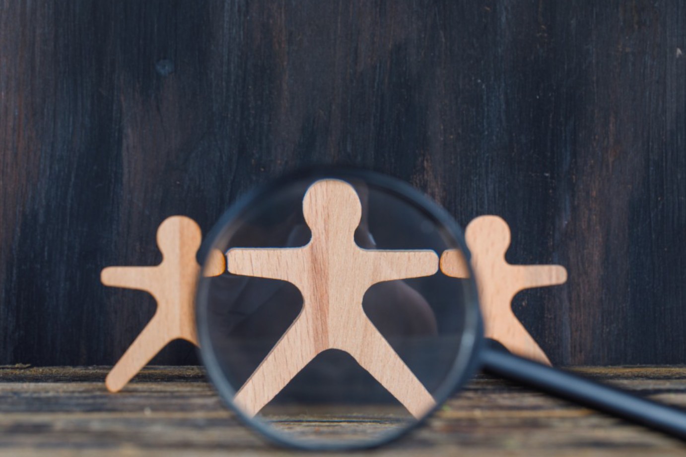 Une loupe se focalise sur une personne en bois parmi trois autres. L’image met en lumière l'importance cruciale de la stratégie commerciale ciblée. Elle souligne la nécessité pour les entreprises de concentrer leurs efforts et leurs ressources sur des segments spécifiques du marché pour maximiser leur efficacité et leur impact.